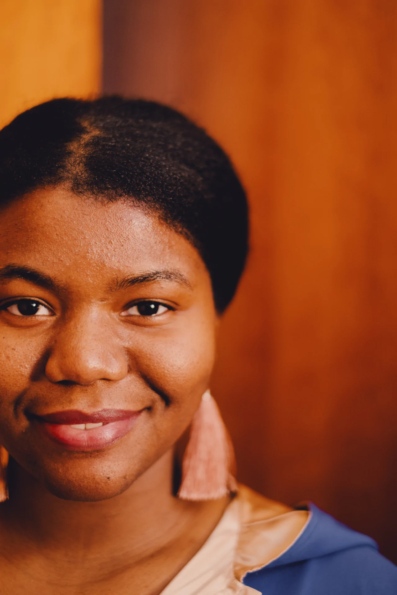 A young african woman smiling in front of a wooden wall.