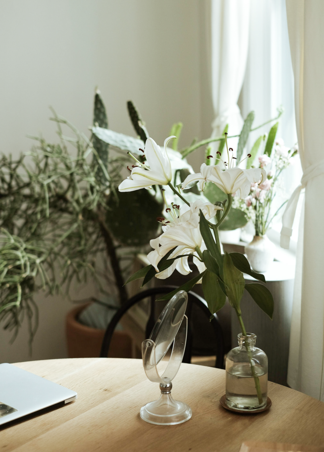 A laptop on a table next to a vase of flowers.
