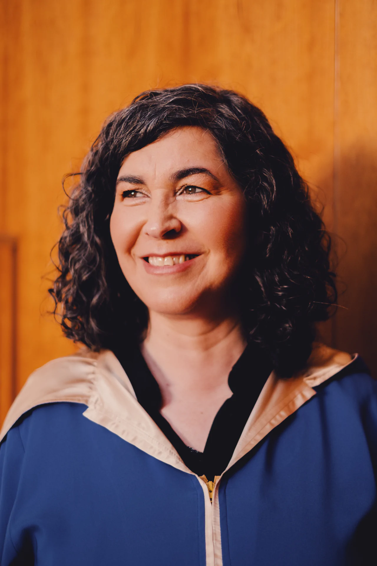A woman in a blue robe smiling in front of a wooden wall.