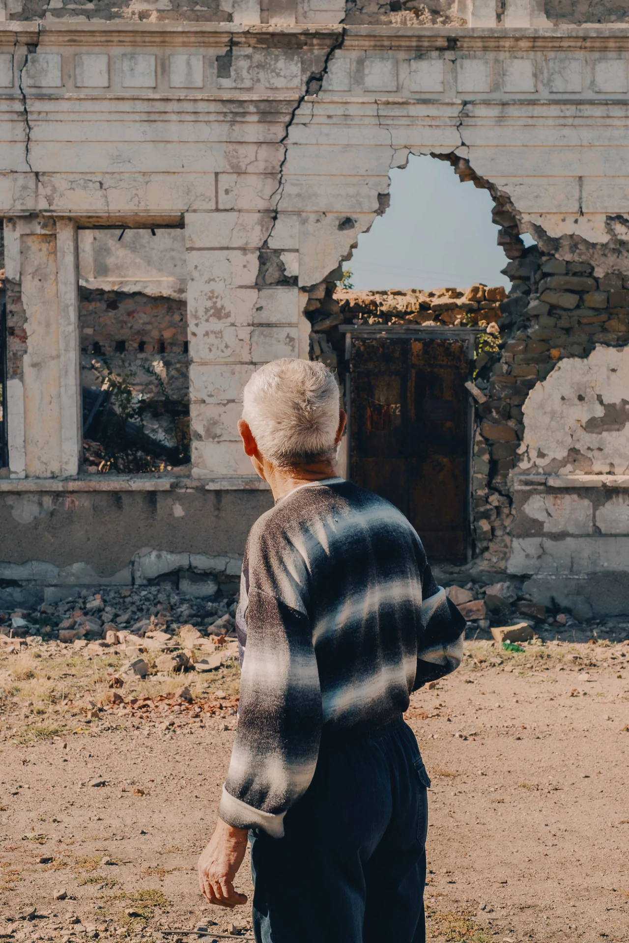 An old man standing in front of a demolished building.