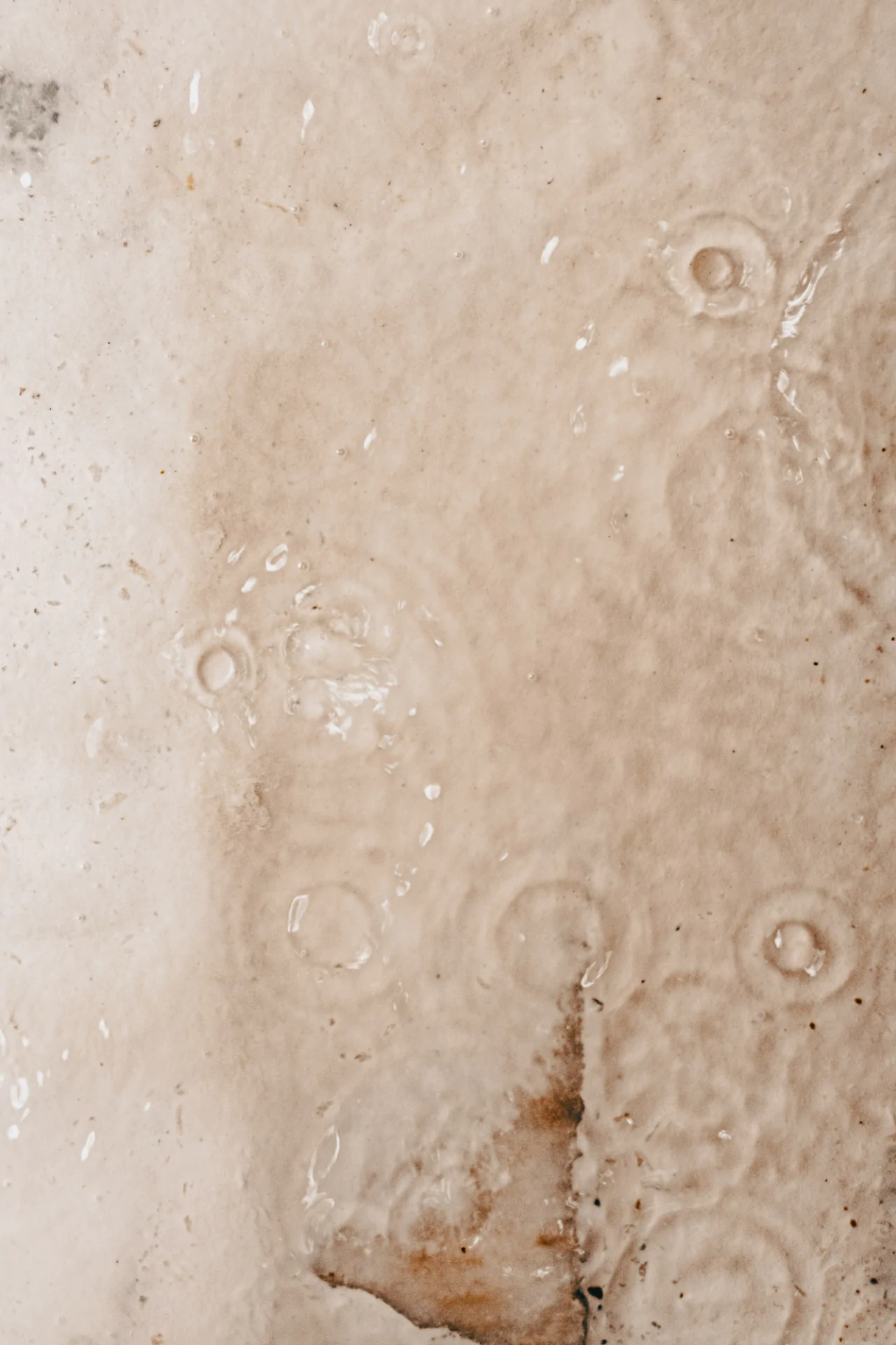 Close-up of water droplets creating circular ripples on a wet, textured beige surface.