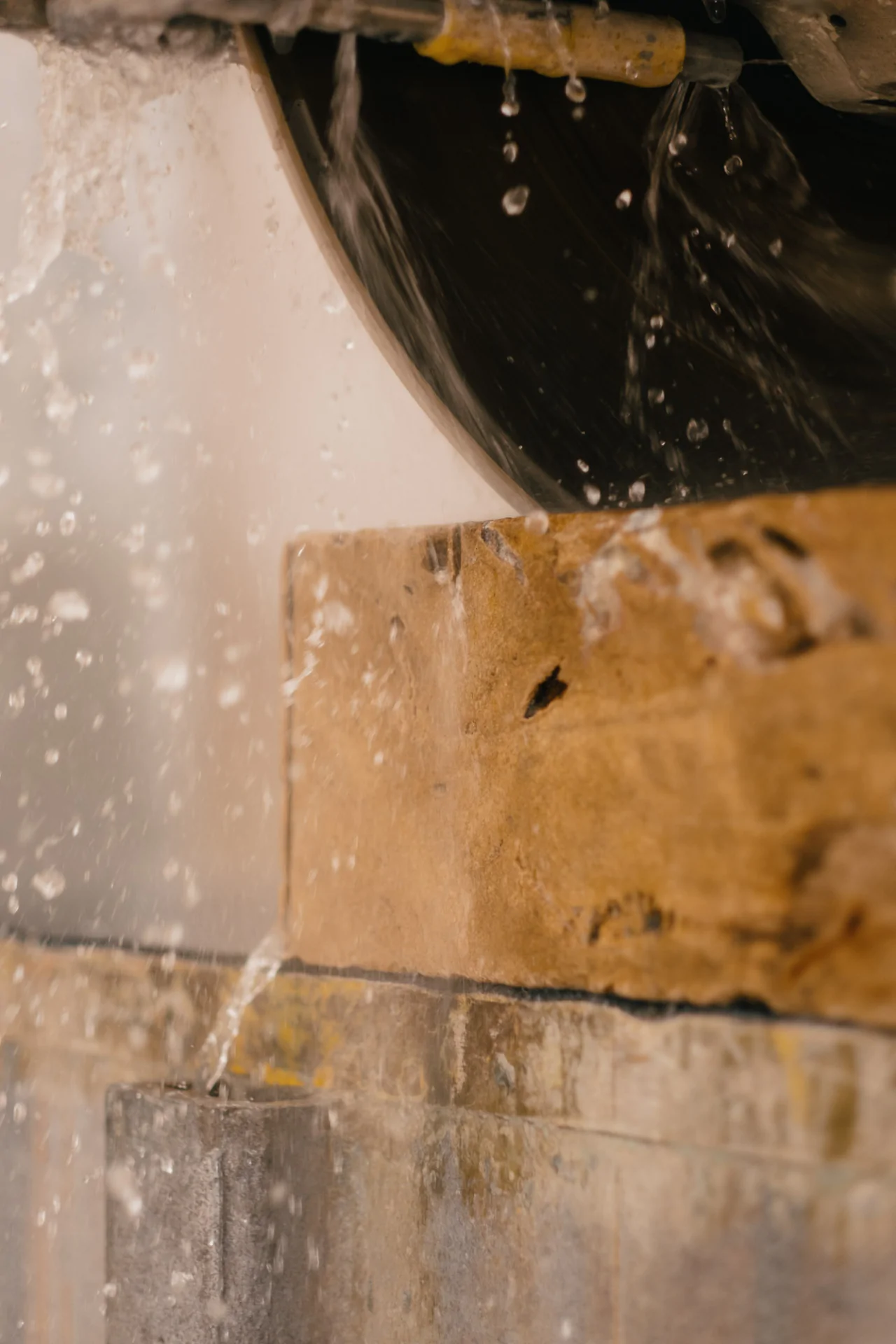 Close-up of a wet saw cutting through a large piece of stone, with water spraying and splashing around the blade.