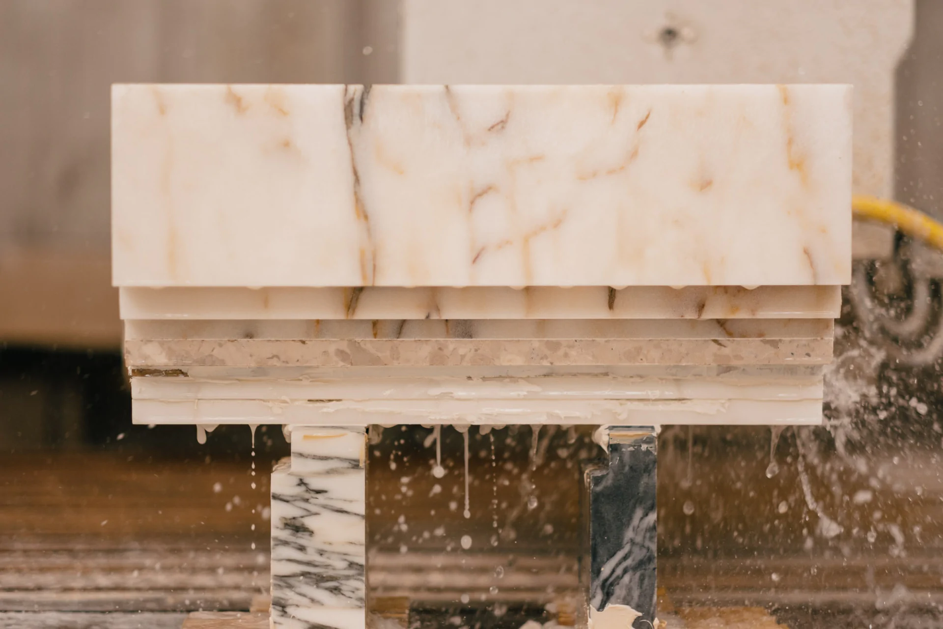 A stack of stone slabs, including marble and granite, with water dripping, displayed on stands in a processing facility.