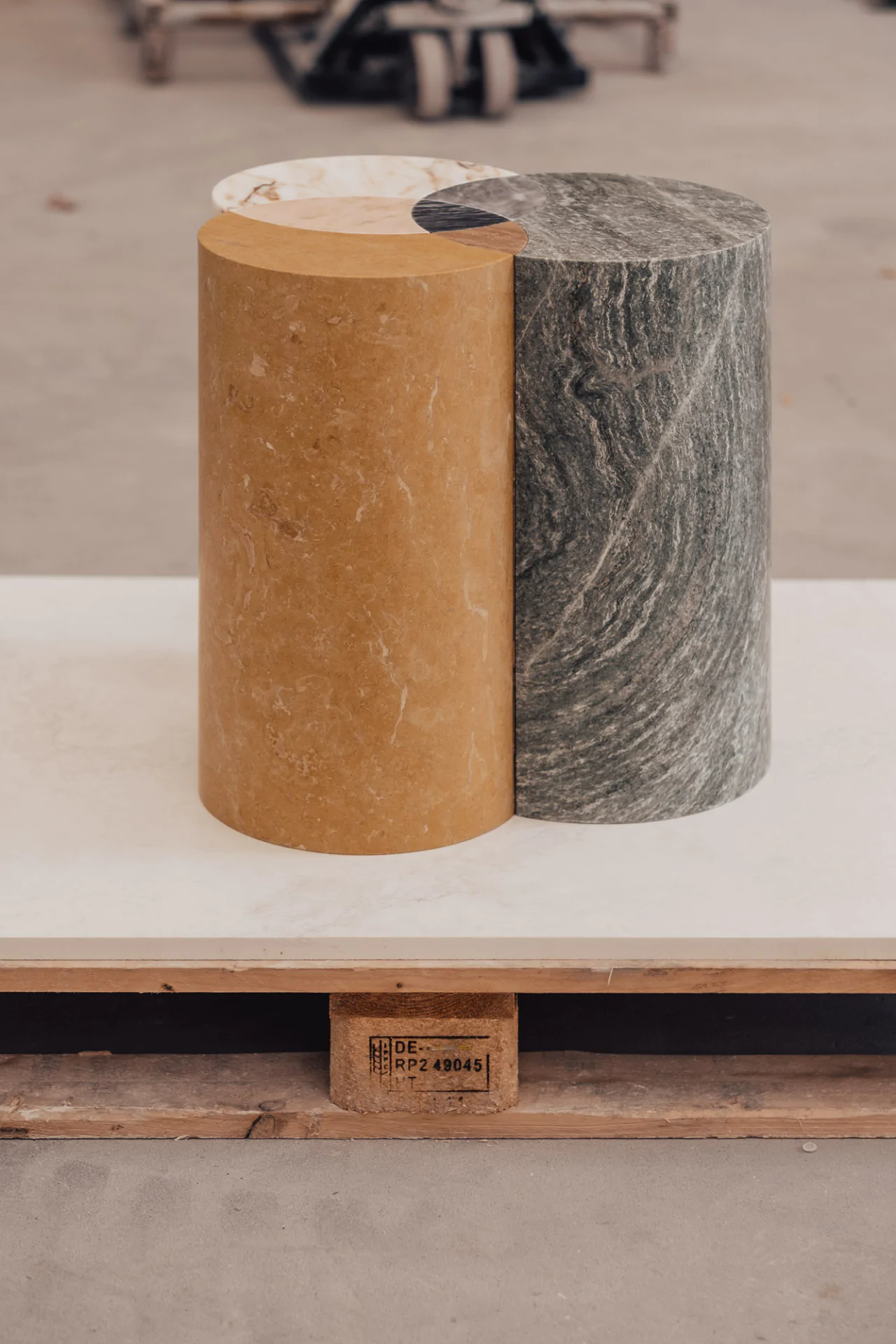 Two cylindrical stone columns, one yellow and one green-gray, placed on a wooden pallet.