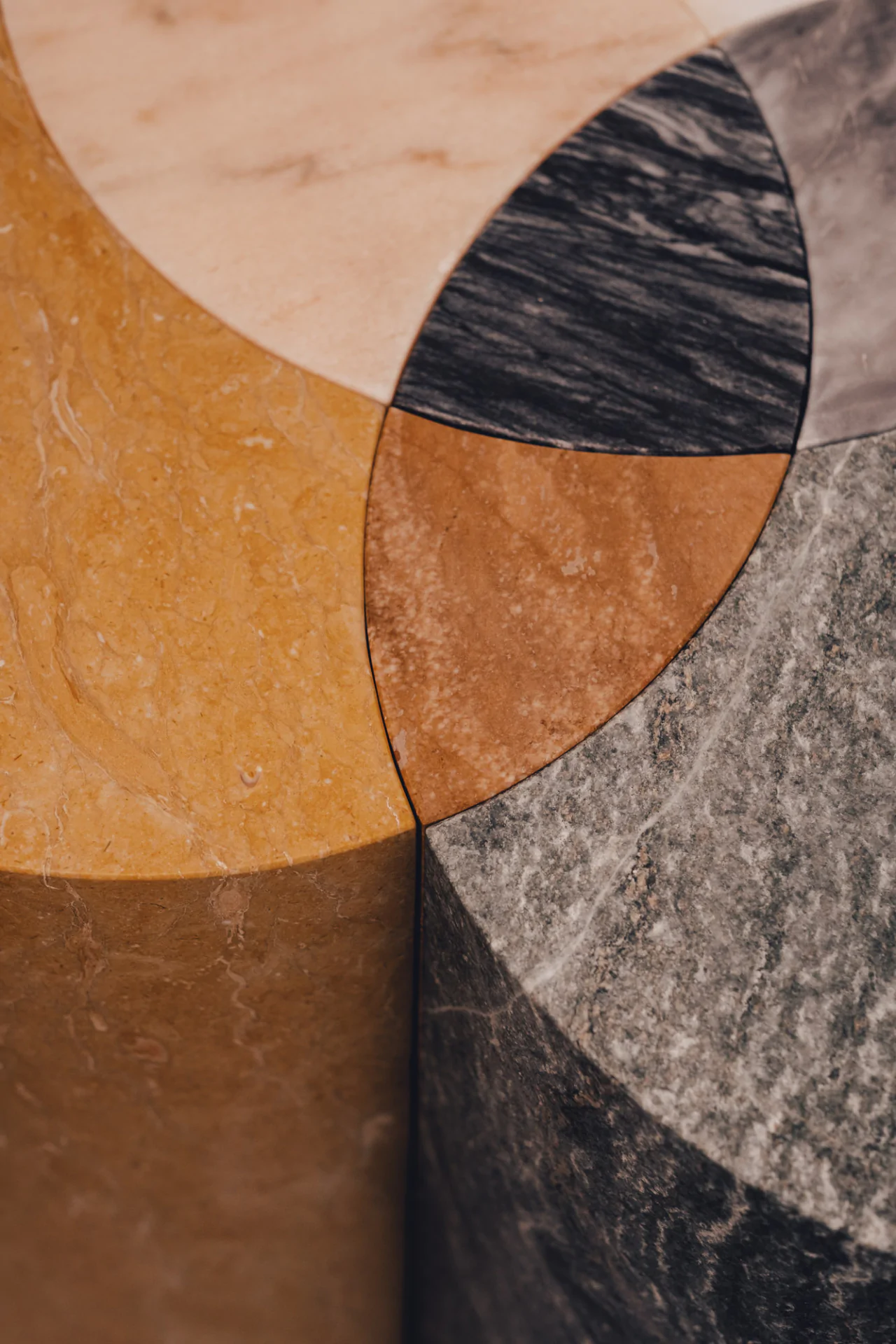 A close-up of a geometric pattern made with colorful marble tiles, including shades of yellow, black, and gray, forming intersecting circular shapes.