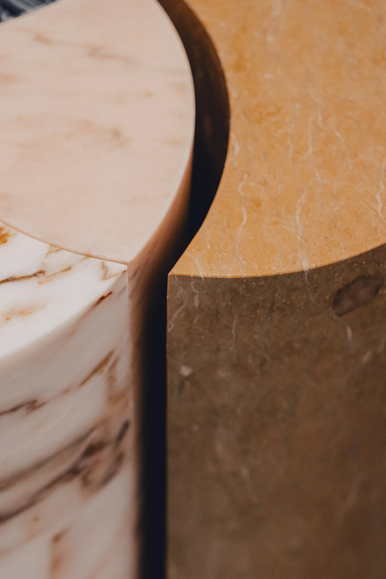 Close-up of two curved stone blocks, one pinkish with white veins, the other brownish with subtle streaks. The blocks are positioned to form a semi-circular gap between them.