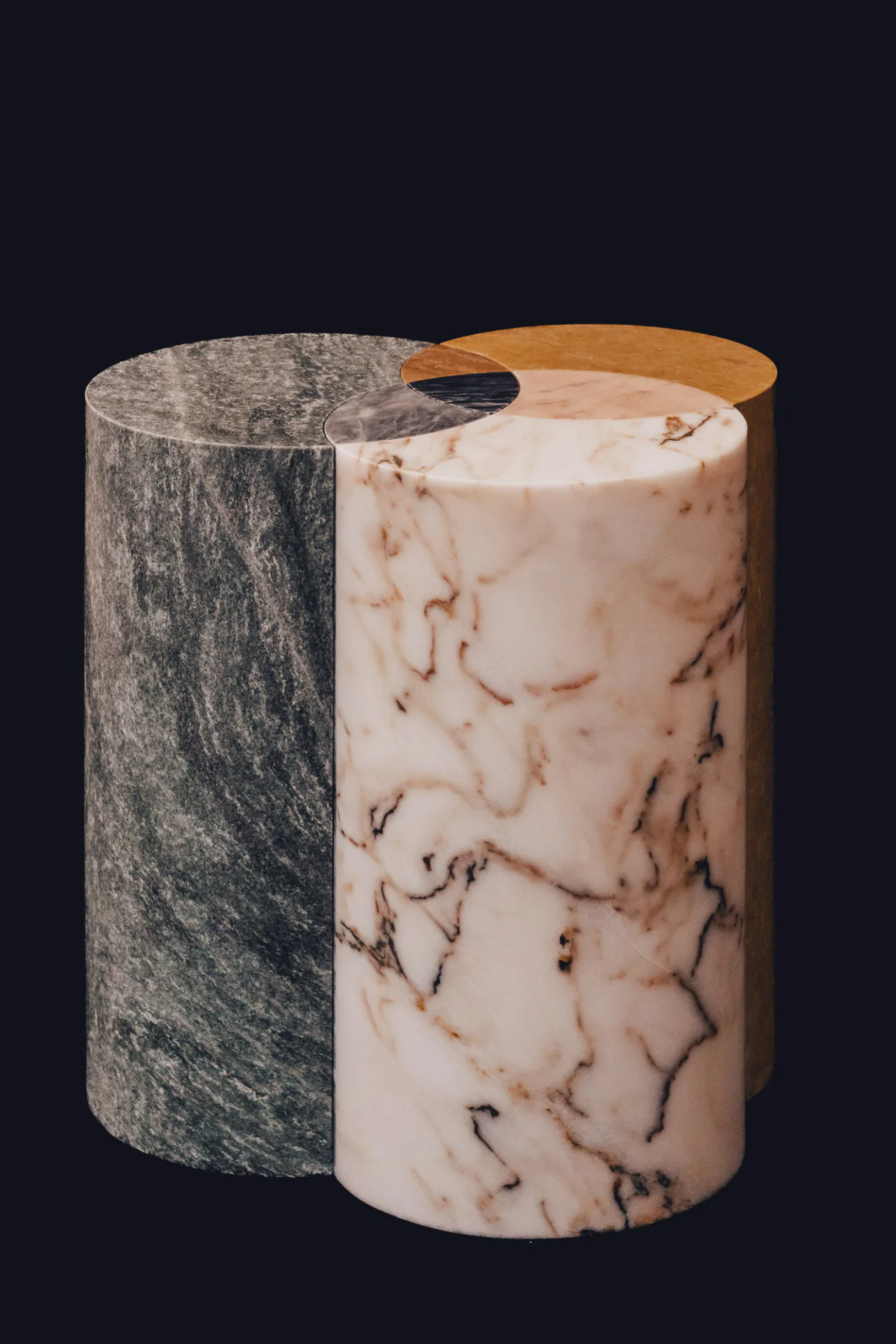 Completed marble table designed by Sebastian Herkner for Cartier Trinity Ring 100th anniversary showing three interlocking sections in different stonesical objects made of green, white with black veins, and tan marble stand together against a black background.