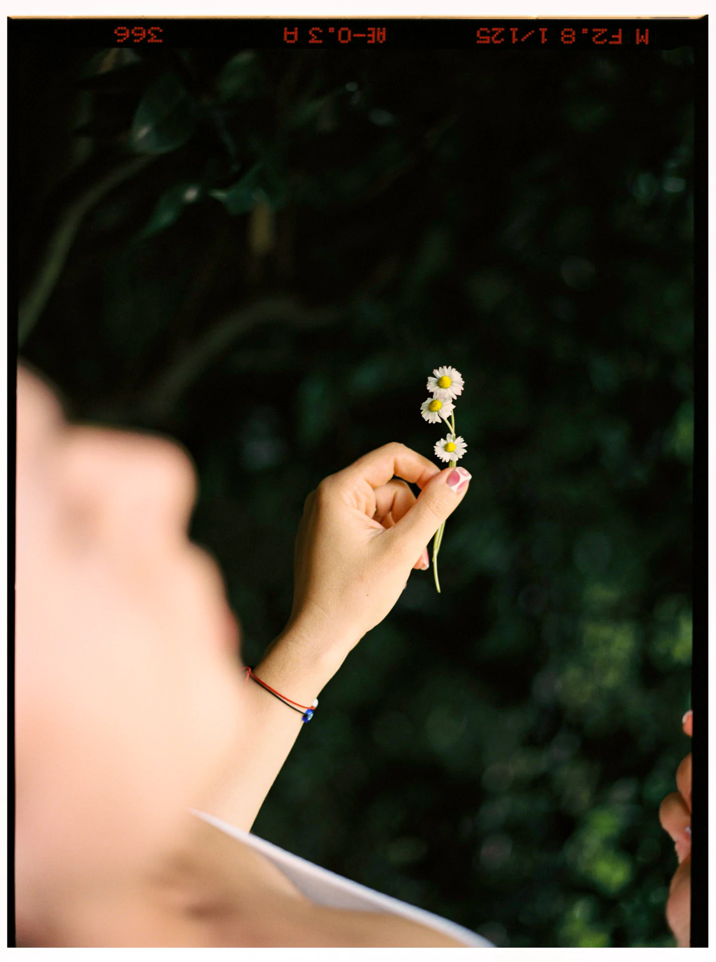 A person lying down holds small white flowers against a dark green background.