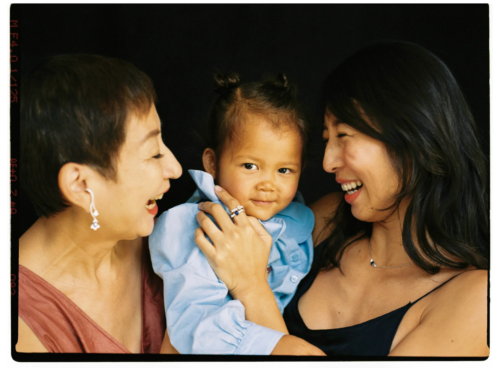 Three people sharing a joyful moment. A child in the center is embraced by two adults on either side, all smiling and happy.