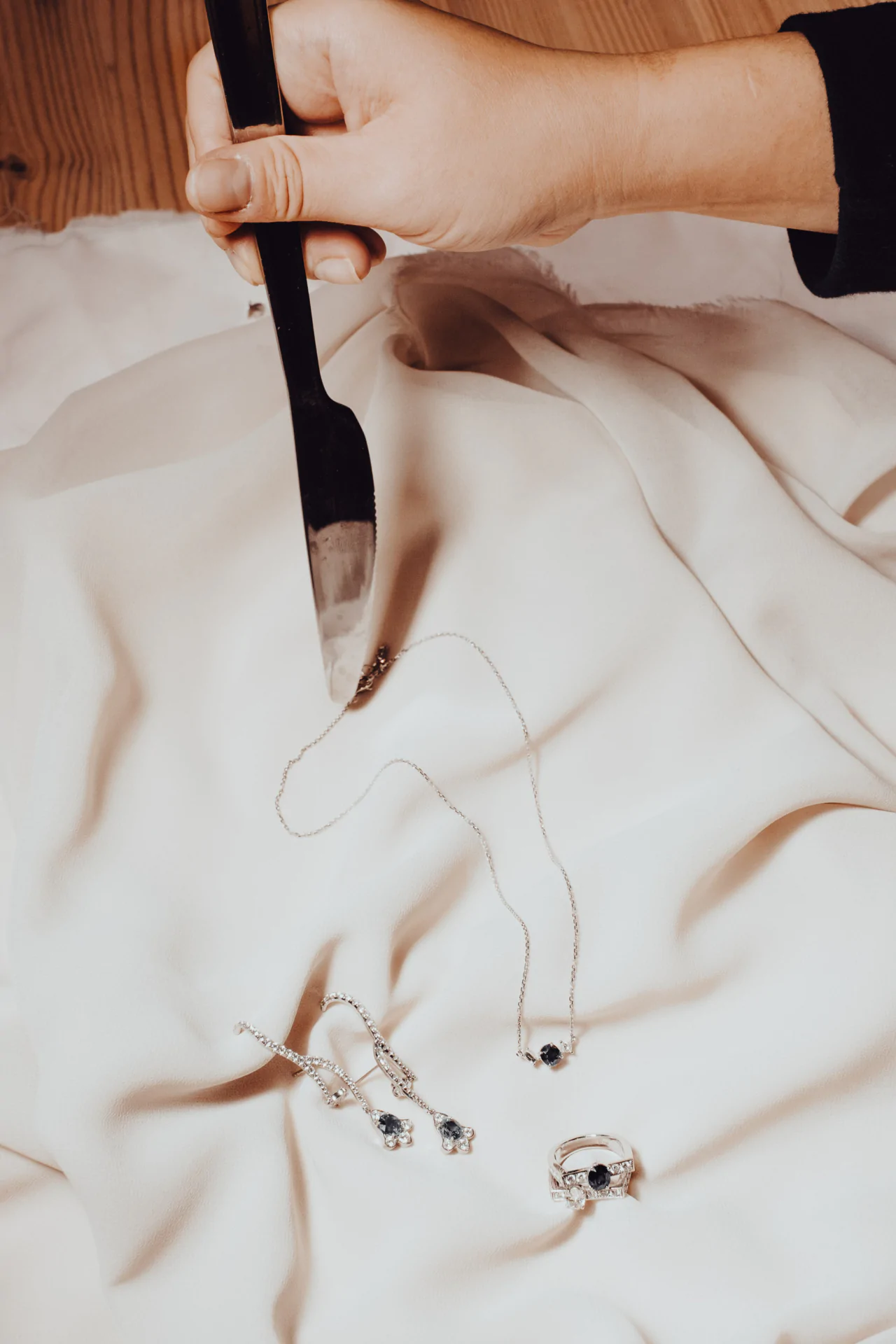 A hand holds a jewelry tool above a cloth displaying a necklace, earrings, and ring, all with dark gemstones.