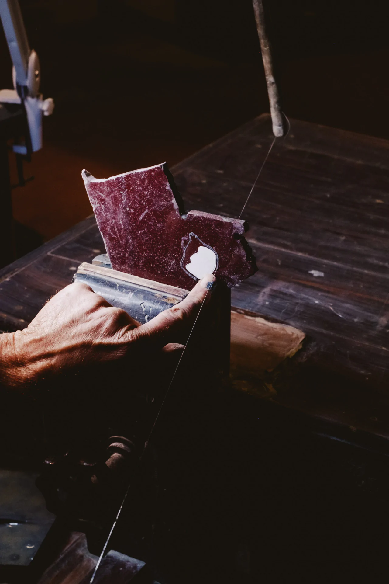 A person guides a red piece of material through a bandsaw on a dark workspace.