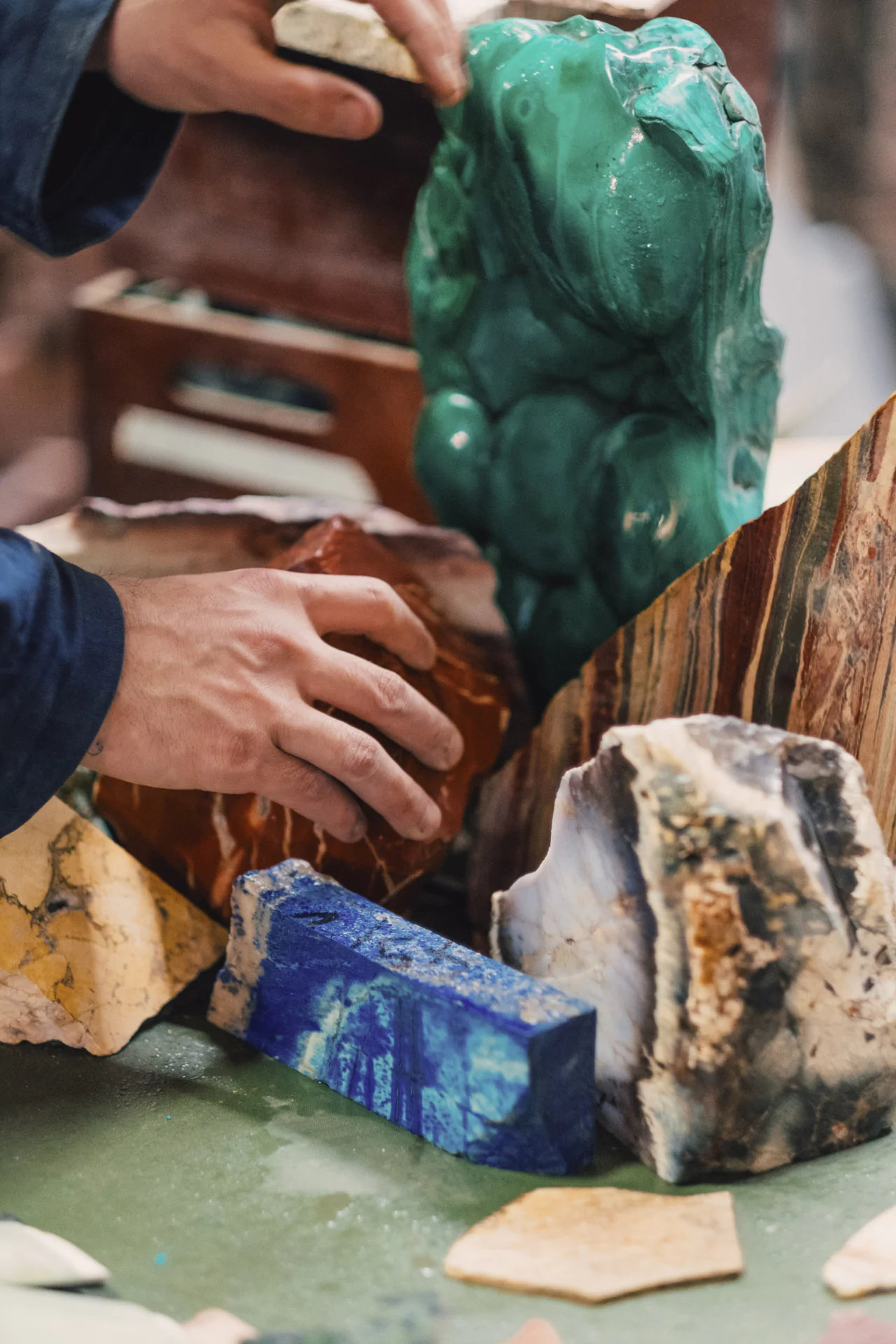Hands arranging various colorful stone sculptures on a surface, including green, blue, red, and striped pieces.