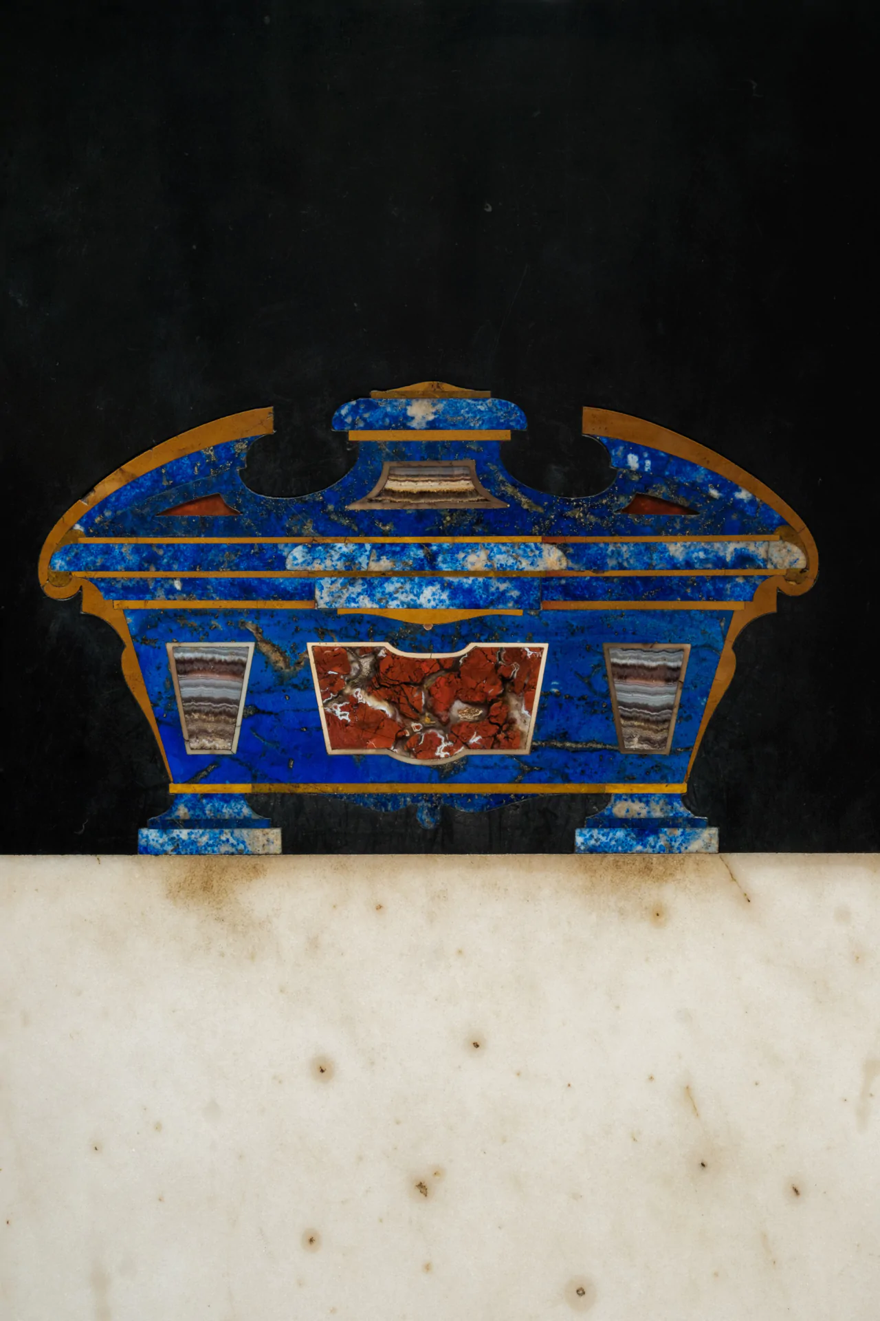A decorative blue and red stone inlay in a rectangular pattern with a marble base against a dark background.