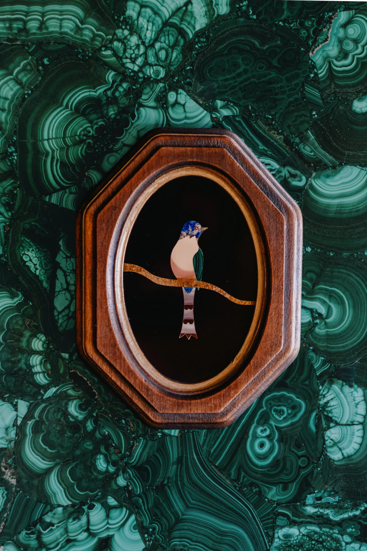 A framed image of a bird on a branch, set against a green malachite-patterned background.