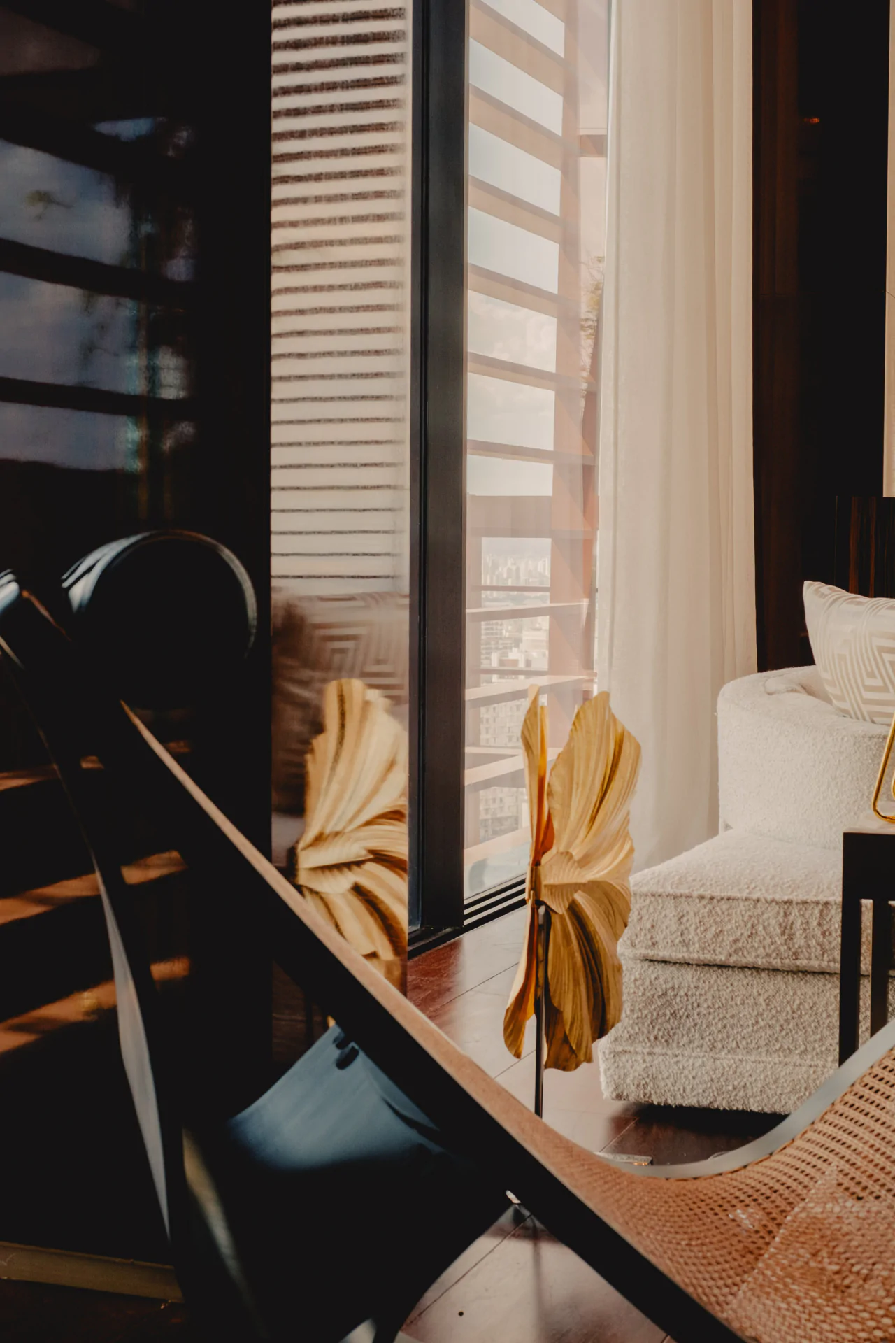 A modern living room with a large window, sheer white curtains, a plush cream sofa, and decorative dried leaves in a vase on a wooden floor—perfect for luxury hotel photography São Paulo.